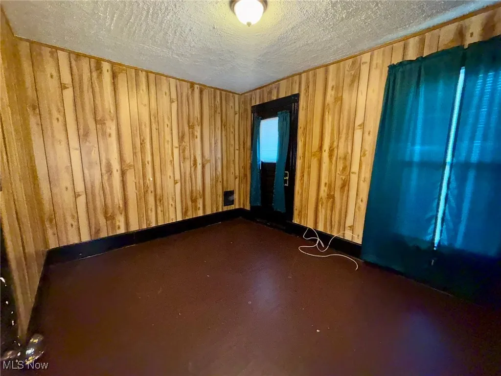 Empty room with wooden walls, finished concrete floors, a textured ceiling and a door to the balcony