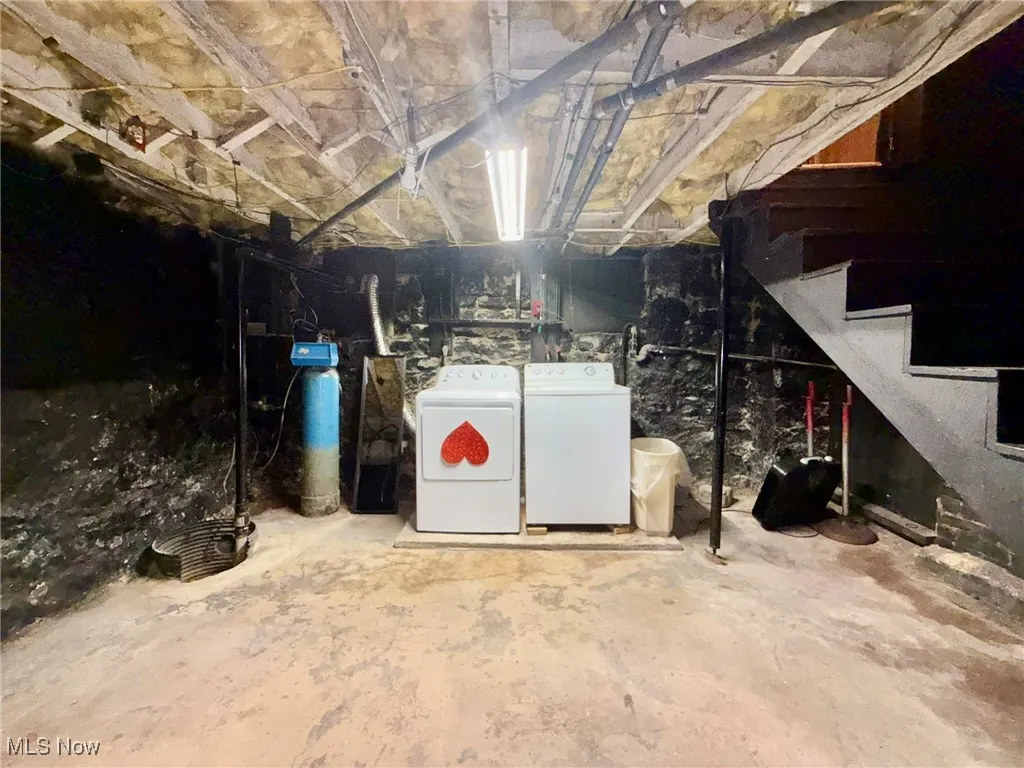 Unfinished below grade area featuring stairs, washer and clothes dryer, and a water softener