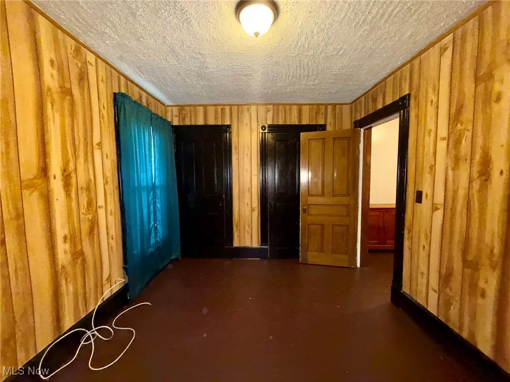 Unfurnished bedroom featuring wood walls, two closets, a textured ceiling, and concrete flooring
