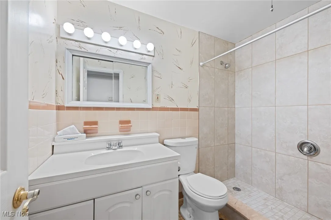 Full bathroom featuring a stall shower, vanity, tile walls, wallpapered walls, and wainscoting
