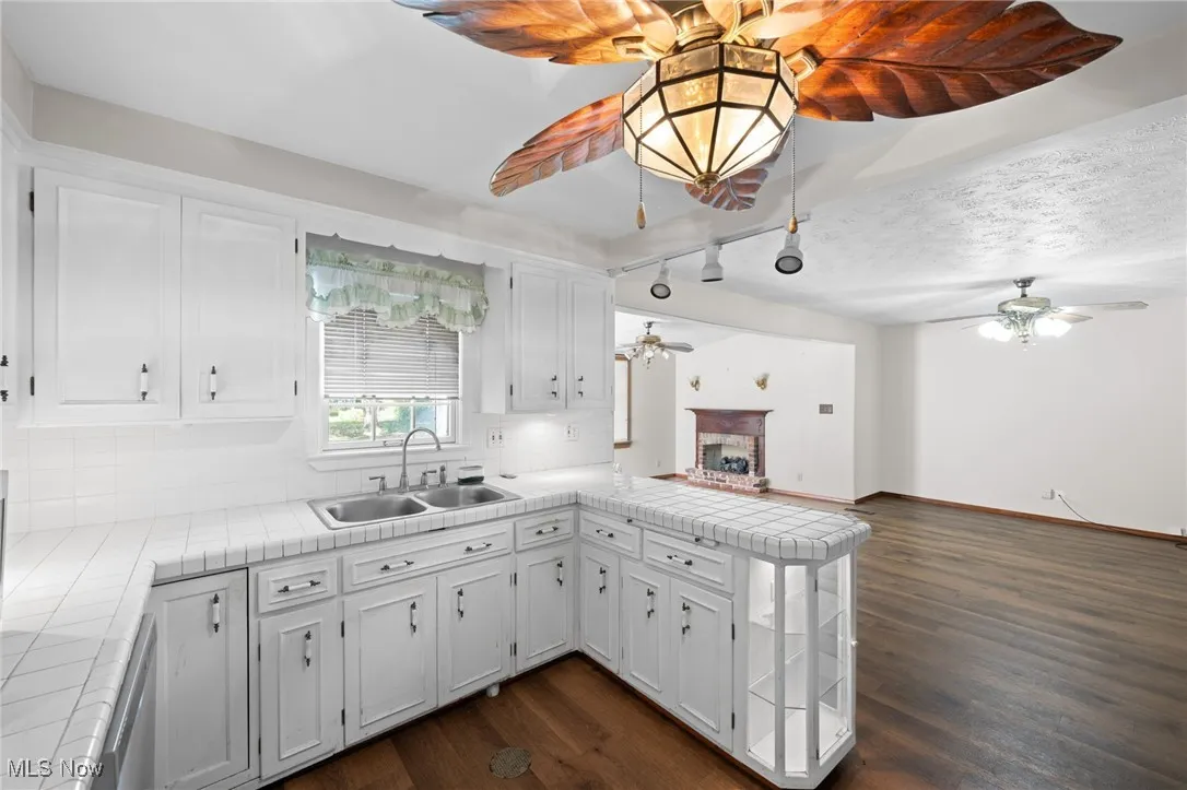 Kitchen featuring tile countertops, a peninsula, a brick fireplace, and white cabinetry