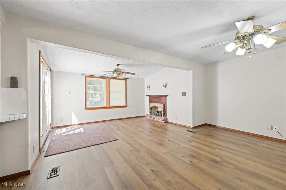 Unfurnished living room with ceiling fan, light wood-style flooring, a fireplace, lofted ceiling, and a textured ceiling