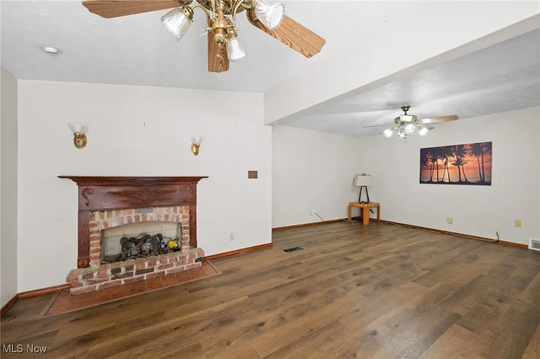 Unfurnished living room with ceiling fan, a textured ceiling, a fireplace, and dark wood-style floors