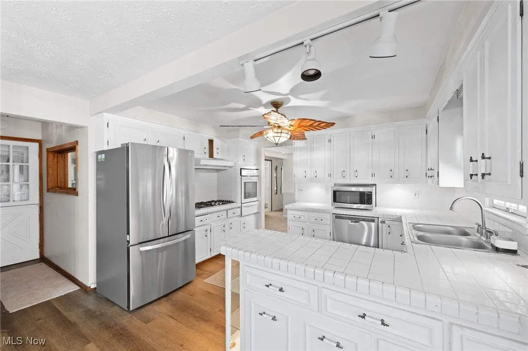 Kitchen with tile countertops, white cabinets, appliances with stainless steel finishes, light wood-type flooring, and a peninsula