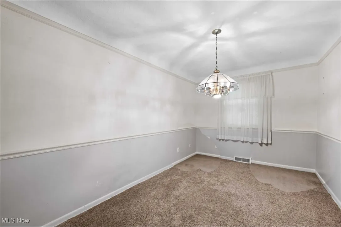 Carpeted empty room with a chandelier and crown molding