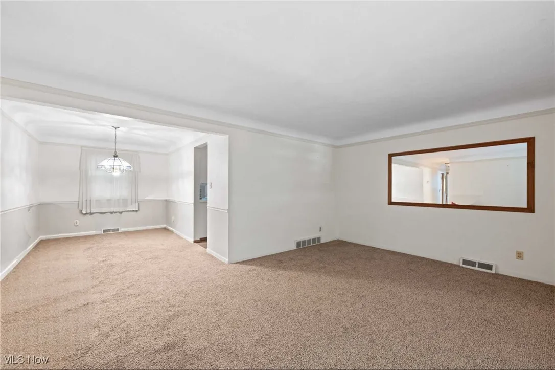 Carpeted spare room featuring ornamental molding and a chandelier