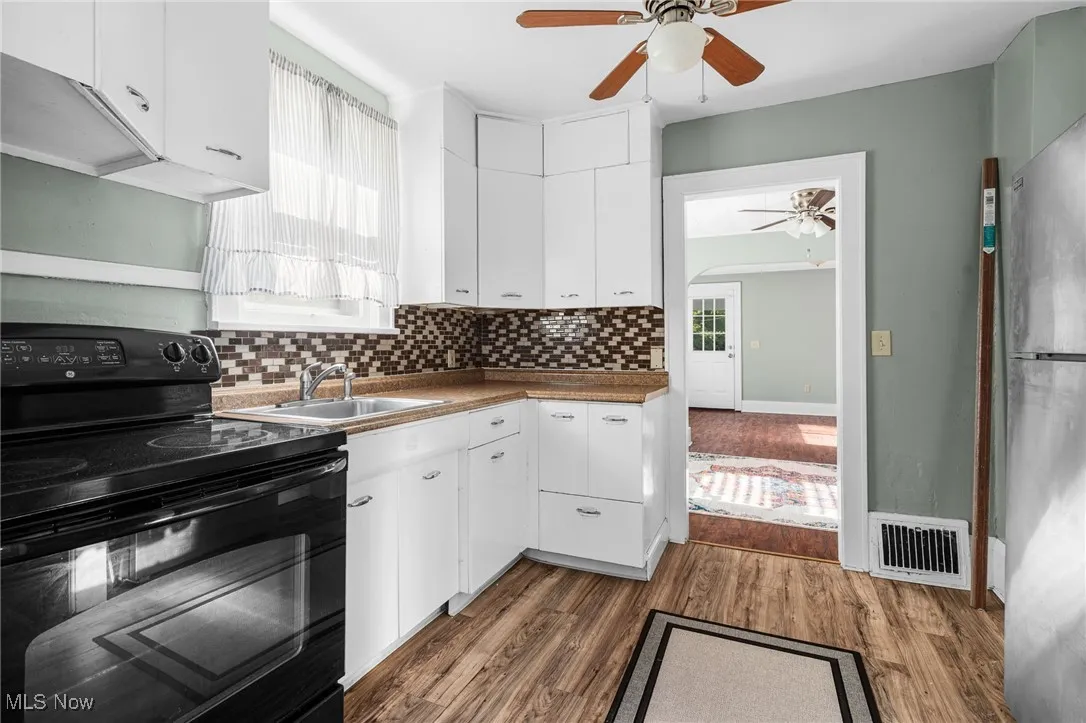 Kitchen featuring electric range, white cabinetry, backsplash, and dark wood-type flooring