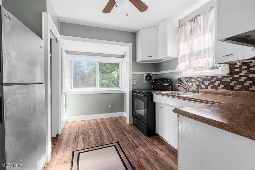 Kitchen with white cabinets, freestanding refrigerator, electric range, and plenty of natural light