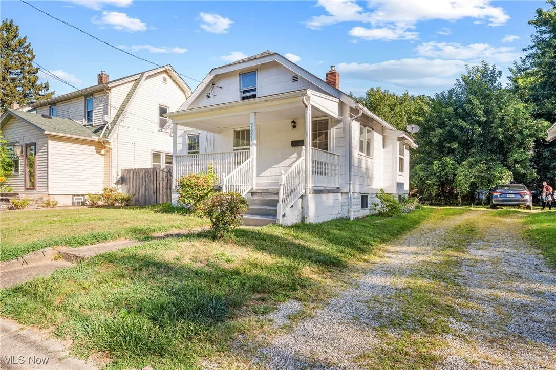 View of front of home featuring driveway, covered porch, a chimney, and a front yard