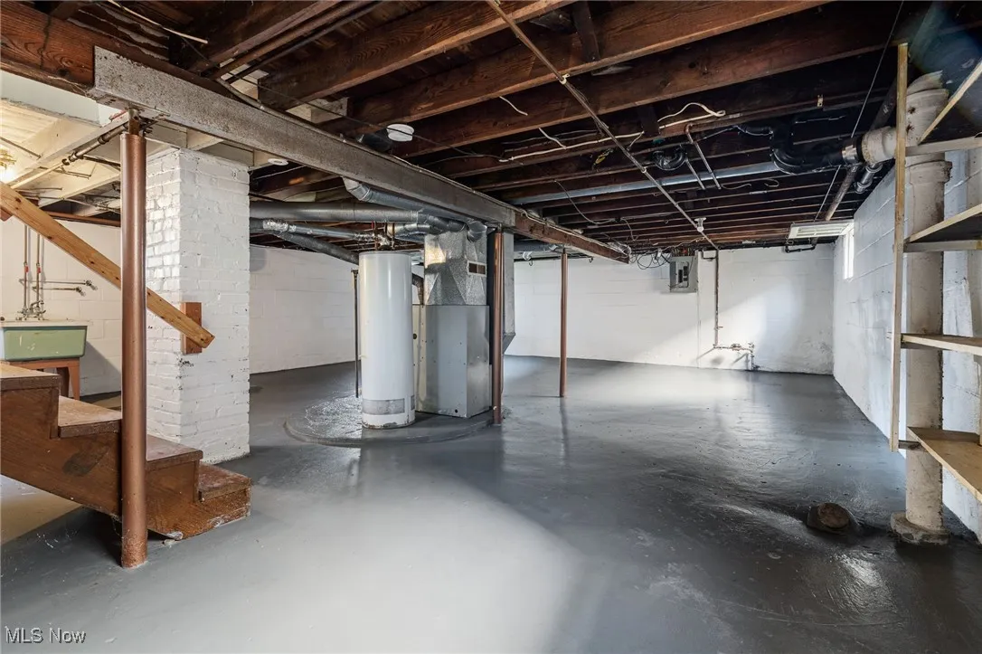 Unfinished basement featuring gas water heater, heating unit, stairs, and electric panel