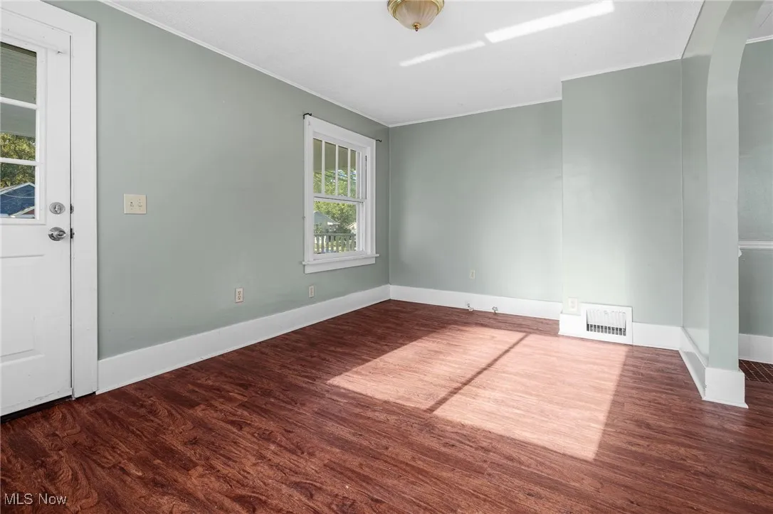 Unfurnished room featuring crown molding, dark wood finished floors, and arched walkways
