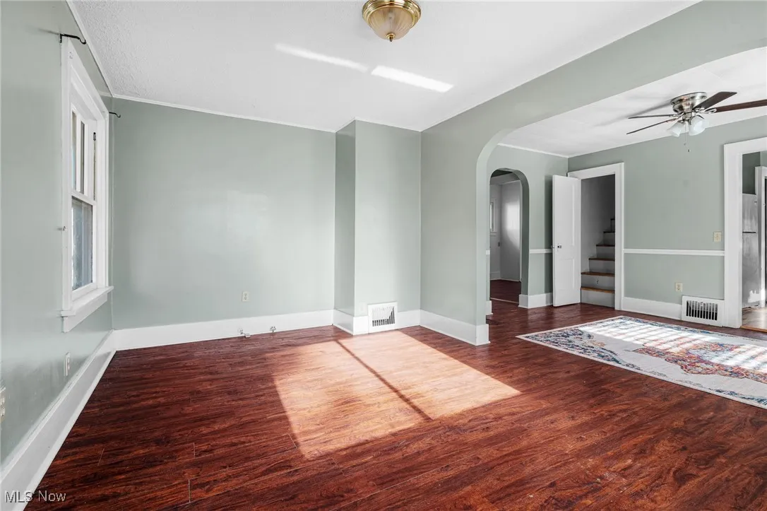 Empty room with dark wood-style floors, a ceiling fan, arched walkways, and stairway