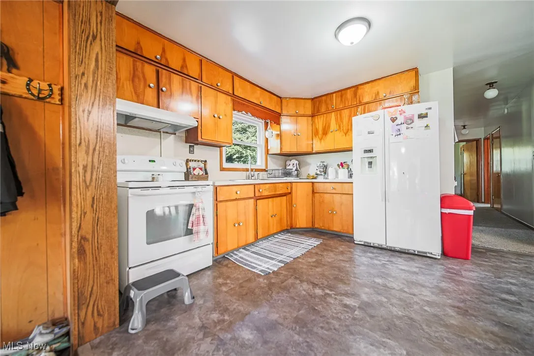 Kitchen with white appliances, light countertops, under cabinet range hood, and brown cabinets