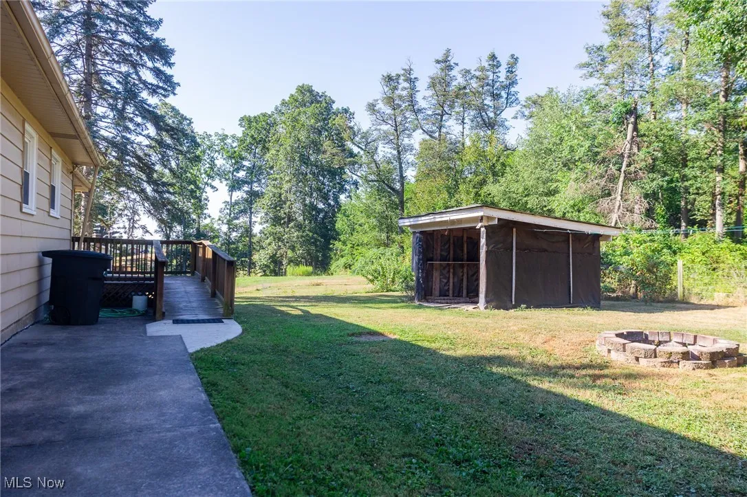 View of green lawn featuring a fire pit and a wooden deck