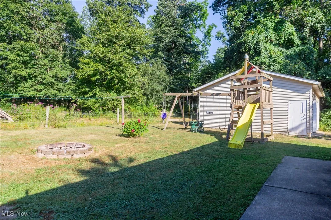 View of yard with a playground, view of wooded area, and an outdoor fire pit