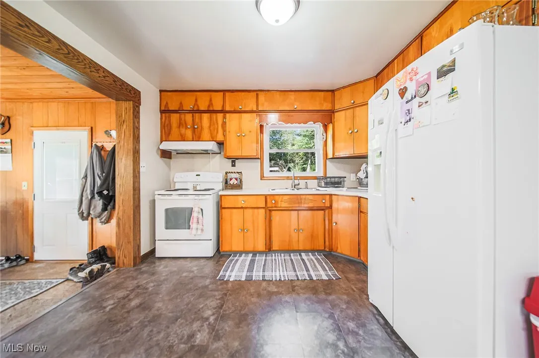 Kitchen featuring white appliances, light countertops, wood walls, under cabinet range hood, and brown cabinetry