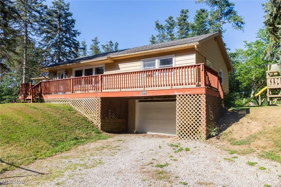 View of front facade with gravel driveway, a garage, a deck, and a playground
