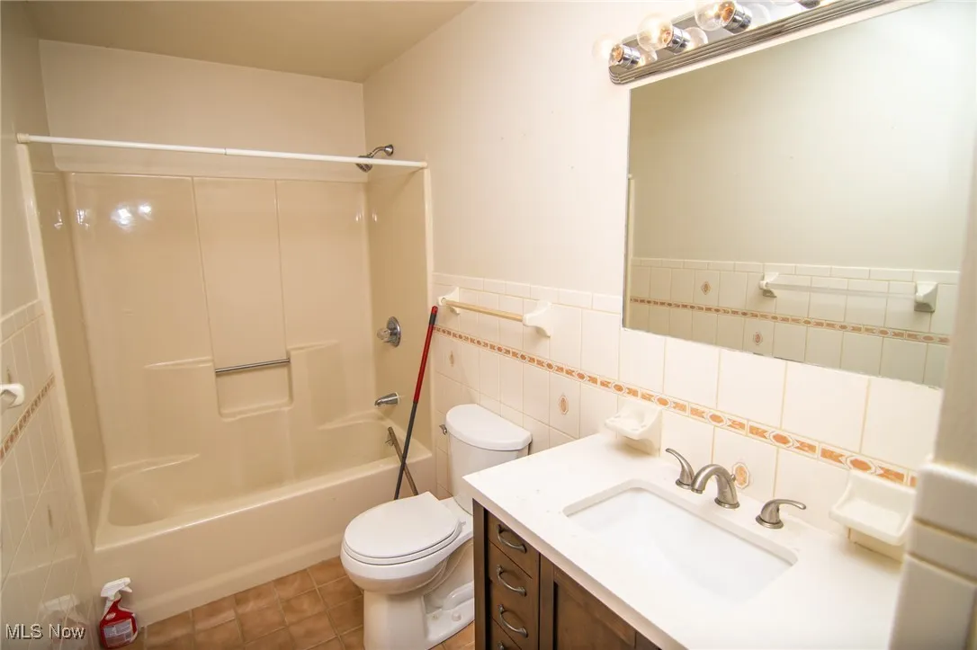 Full bathroom with tile walls, shower / bathtub combination, vanity, light tile patterned flooring, and a wainscoted wall