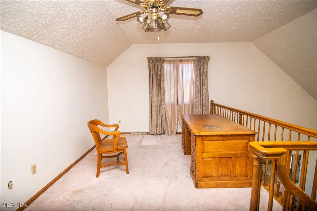 Office featuring a textured ceiling, light colored carpet, vaulted ceiling, and a ceiling fan