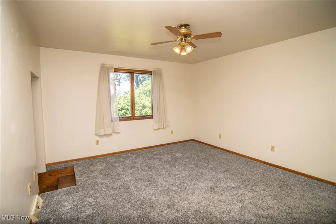 Carpeted empty room featuring ceiling fan and baseboards