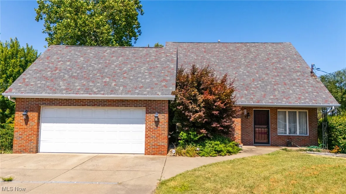 View of front facade featuring a front lawn, concrete driveway, brick siding, and roof with shingles