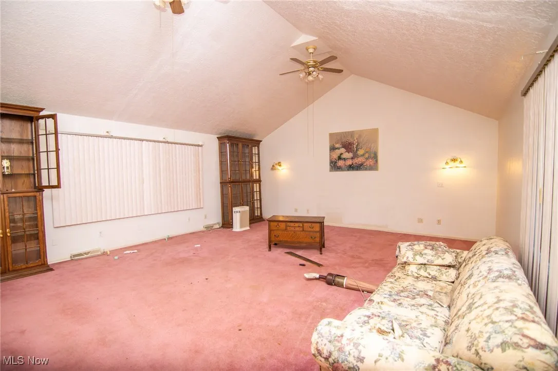 Living area with a textured ceiling, carpet, a ceiling fan, and vaulted ceiling