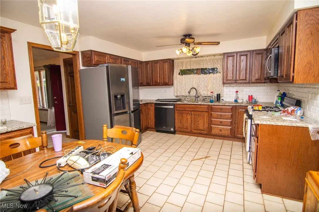 Kitchen featuring light stone counters, stainless steel appliances, tasteful backsplash, and brown cabinetry