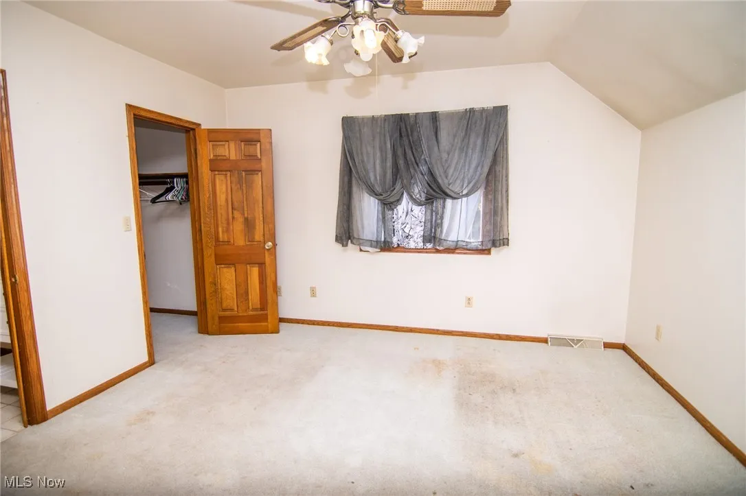 Unfurnished bedroom featuring carpet floors, a spacious closet, ceiling fan, and lofted ceiling