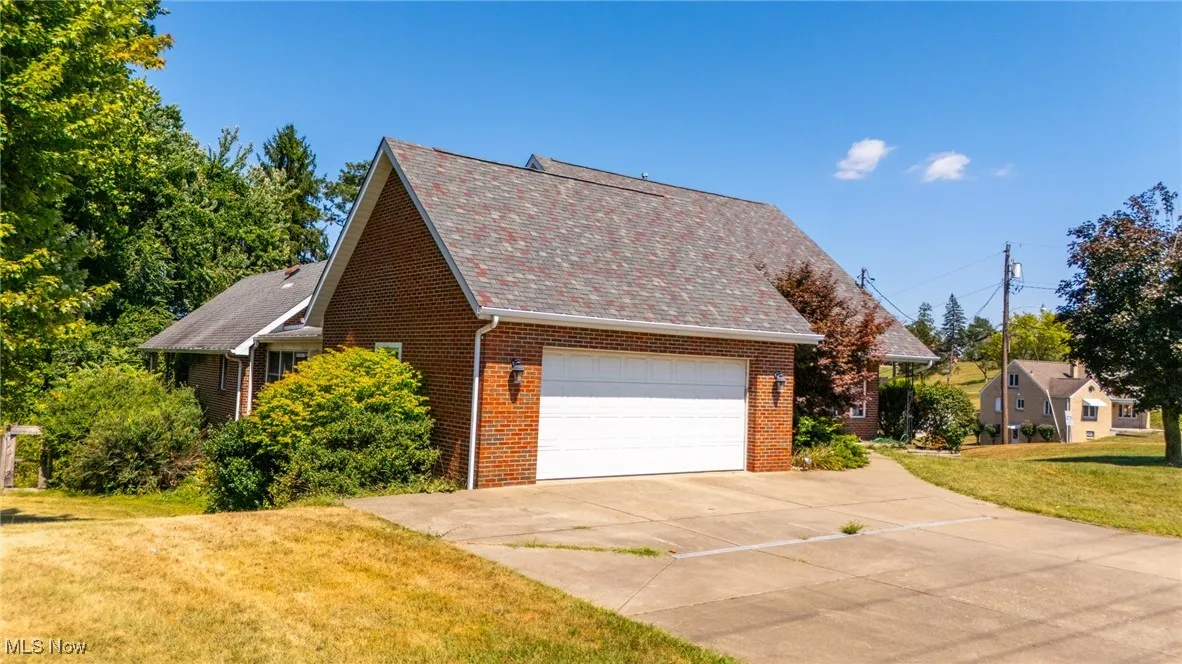 View of property exterior featuring brick siding, concrete driveway, an attached garage, a lawn, and a shingled roof