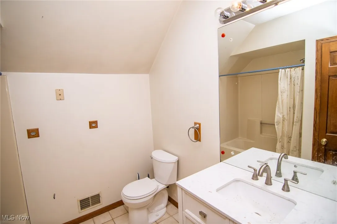 Full bath with light tile patterned floors, vanity, vaulted ceiling, and shower / bath combination with curtain