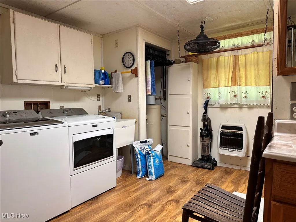 Washroom featuring light wood-type flooring, heating unit, cabinet space, and washer and clothes dryer