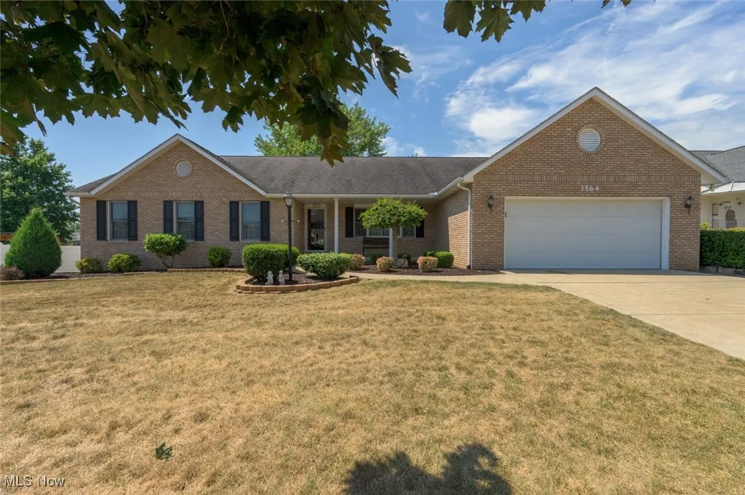 Ranch-style home with a porch, a garage, a front yard, concrete driveway, and brick siding