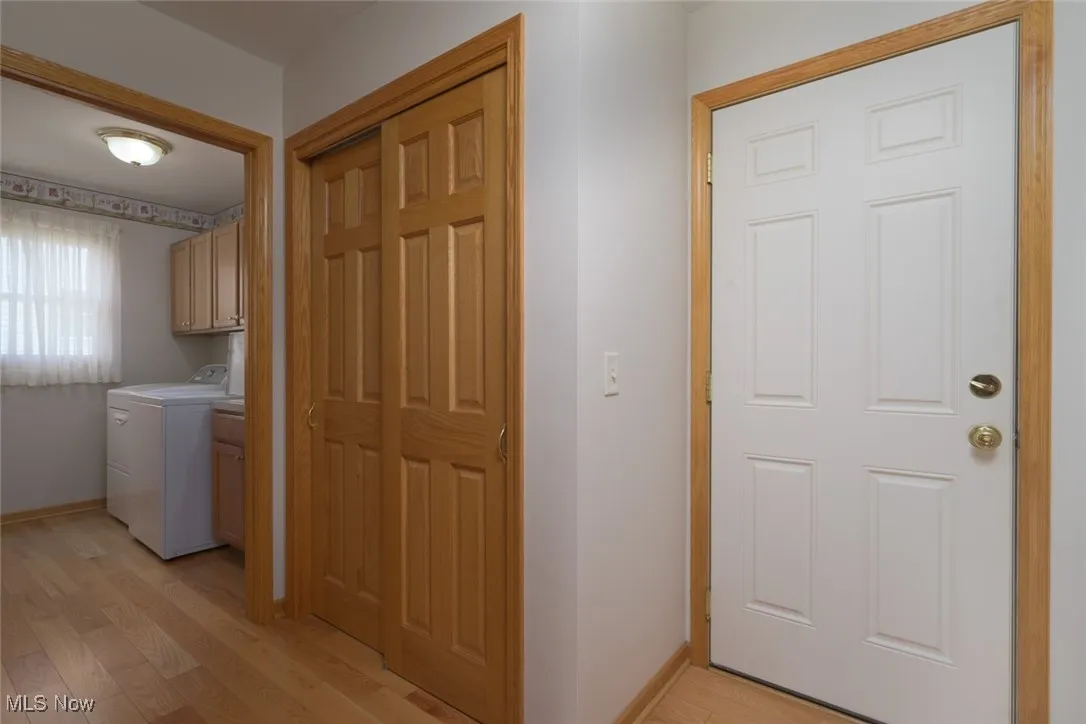 Laundry area with light wood finished floors, cabinet space, and washer and clothes dryer