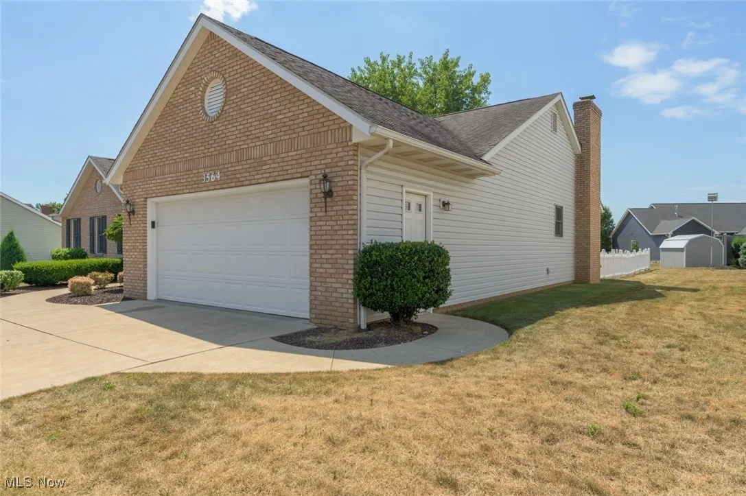 View of home's exterior with brick siding, a garage, a lawn, driveway, and roof with shingles