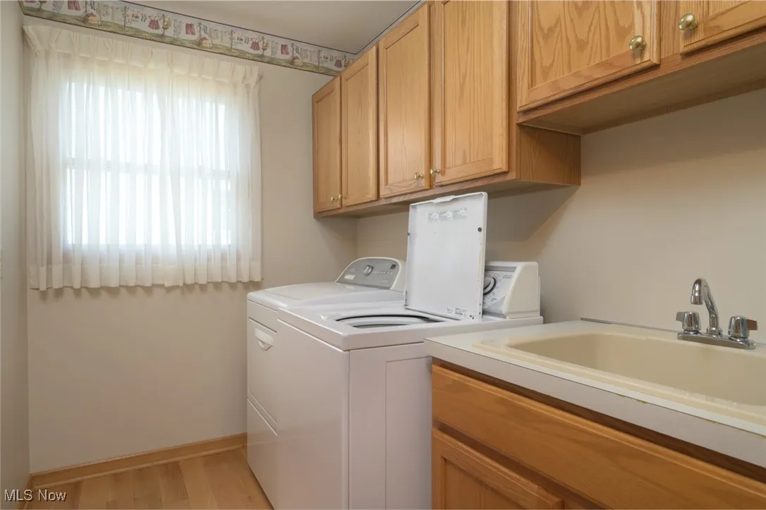 Washroom with light wood-style flooring, separate washer and dryer, and cabinet space