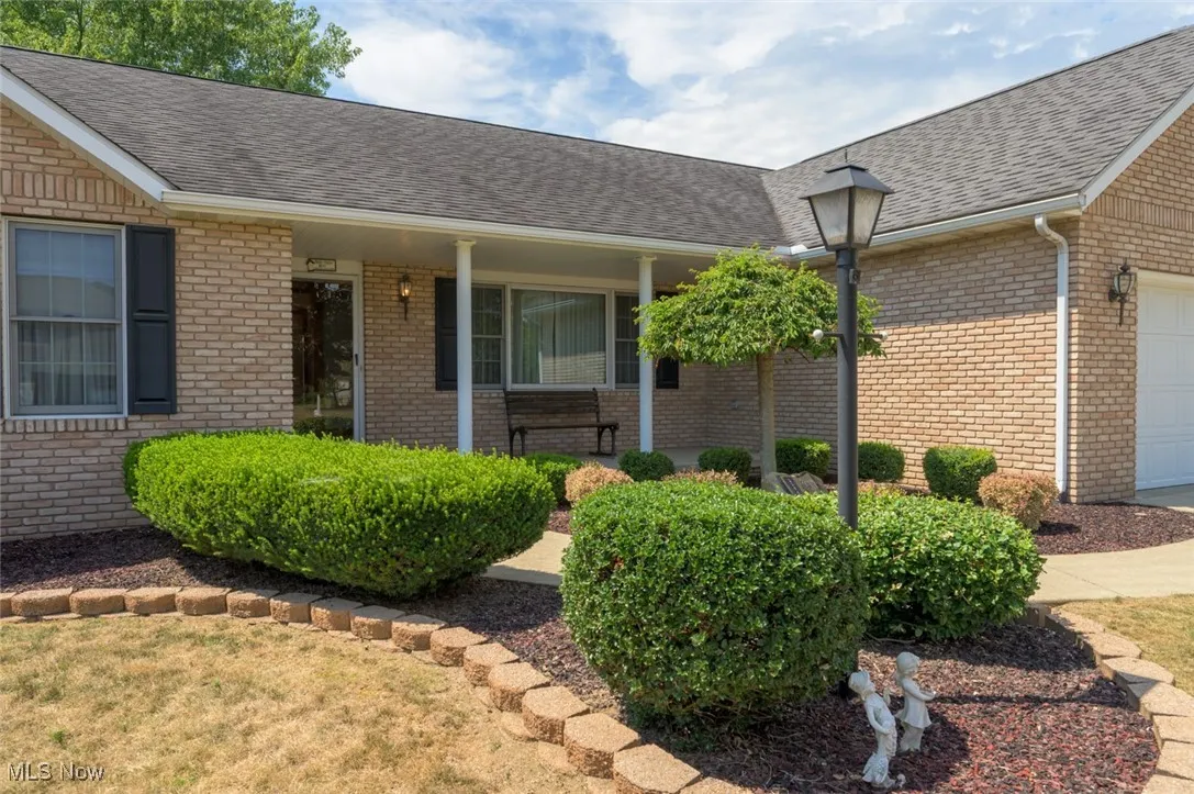 Property entrance featuring covered porch, a shingled roof, and brick siding