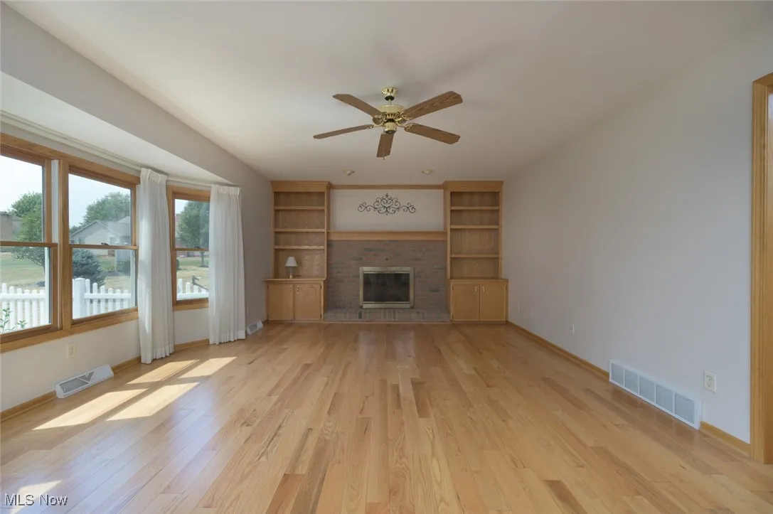 Unfurnished living room with a fireplace, light wood finished floors, ceiling fan, and built in shelves