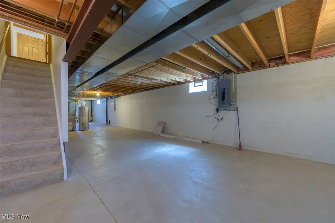 Basement with stairway, electric panel, and gas water heater