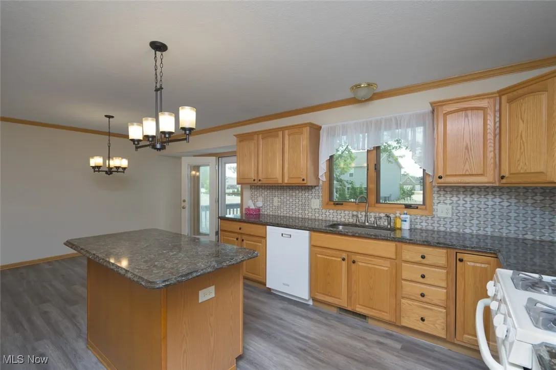 Kitchen featuring white appliances, ornamental molding, tasteful backsplash, dark wood-type flooring, and pendant lighting