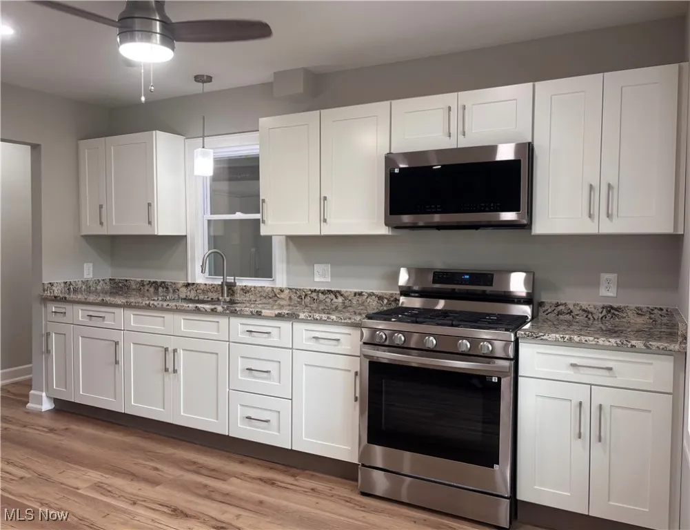 Kitchen featuring appliances with stainless steel finishes, white cabinets, light stone countertops, and light wood finished floors