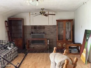 Living room featuring a textured ceiling, wood finished floors, vaulted ceiling, and a fireplace