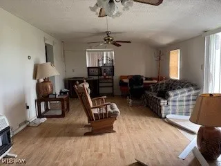 Living area with a textured ceiling, vaulted ceiling, wood finished floors, heating unit, and ceiling fan