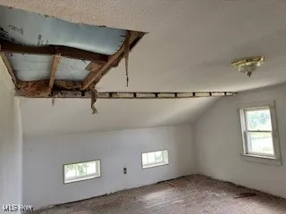 Additional living space with a textured ceiling and vaulted ceiling