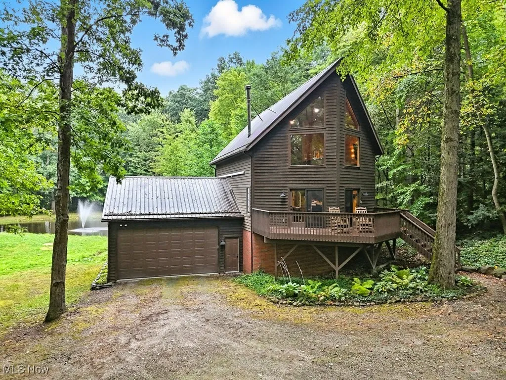 View of front of home featuring dirt driveway, a deck with water view, a metal roof, stairs, and a wooded view