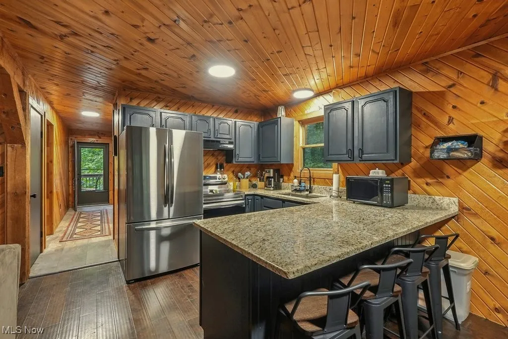 Kitchen featuring wooden walls, appliances with stainless steel finishes, dark wood finished floors, a kitchen breakfast bar, and a peninsula