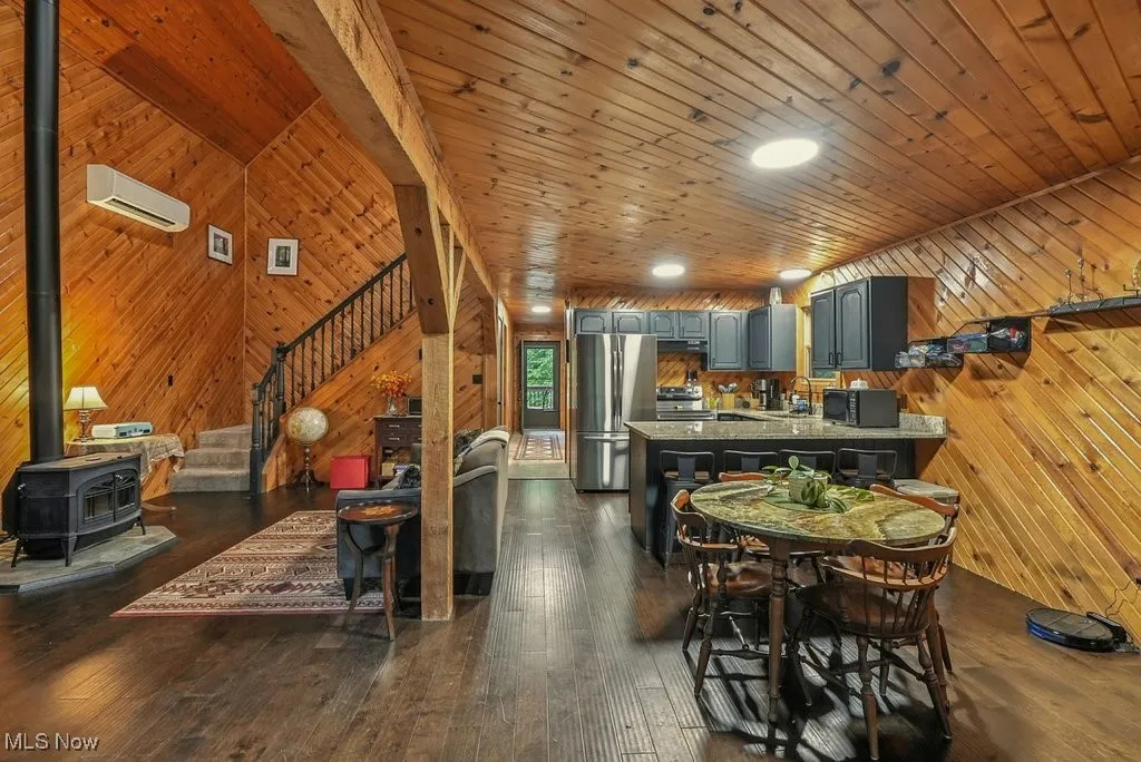 Dining area featuring wooden walls, stairway, a wood stove, dark wood finished floors, and a wall unit AC