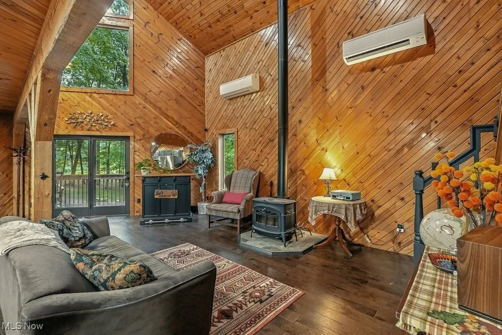 Living area with high vaulted ceiling, a wood stove, wood walls, wood ceiling, and hardwood / wood-style flooring