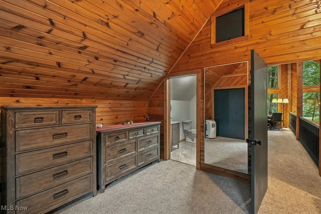 Unfurnished bedroom with lofted ceiling, light colored carpet, wood ceiling, and wooden walls