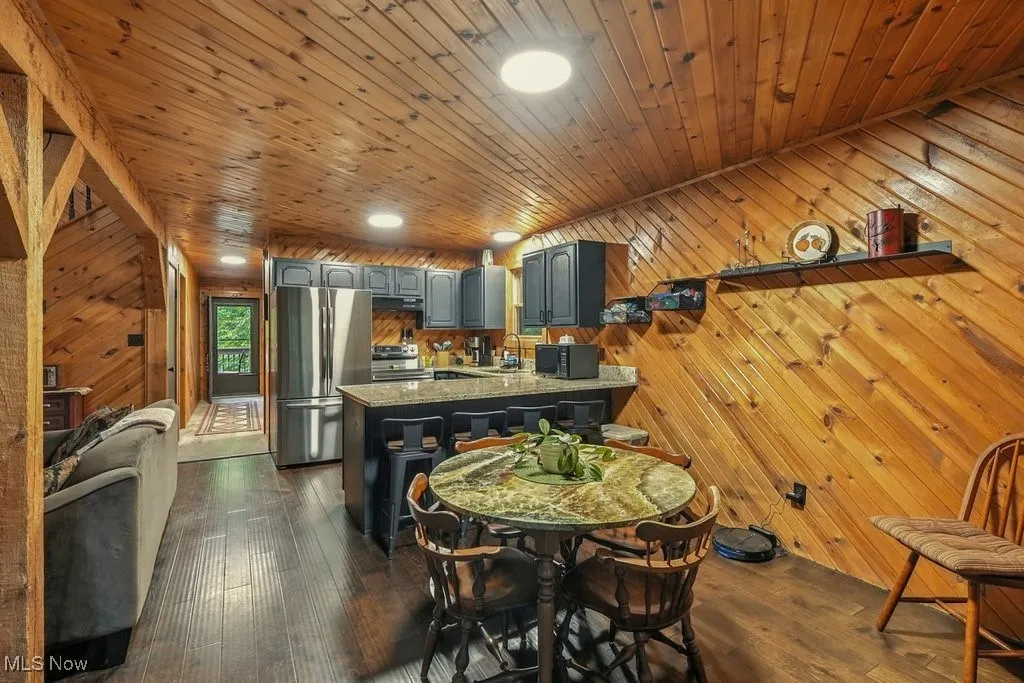 Kitchen featuring wood walls, a peninsula, dark wood finished floors, light stone counters, and appliances with stainless steel finishes