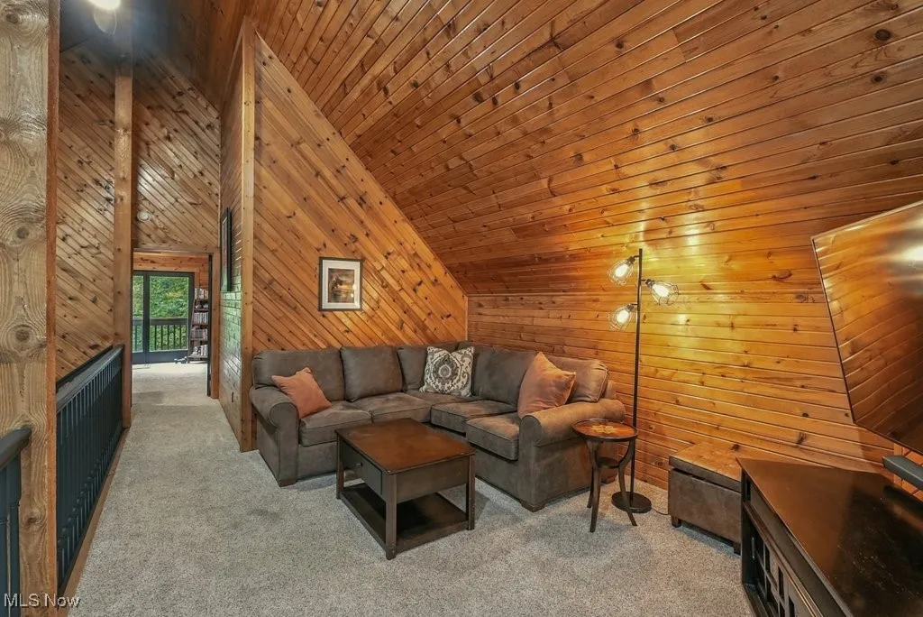 Living room with high vaulted ceiling, carpet, wood walls, and wooden ceiling